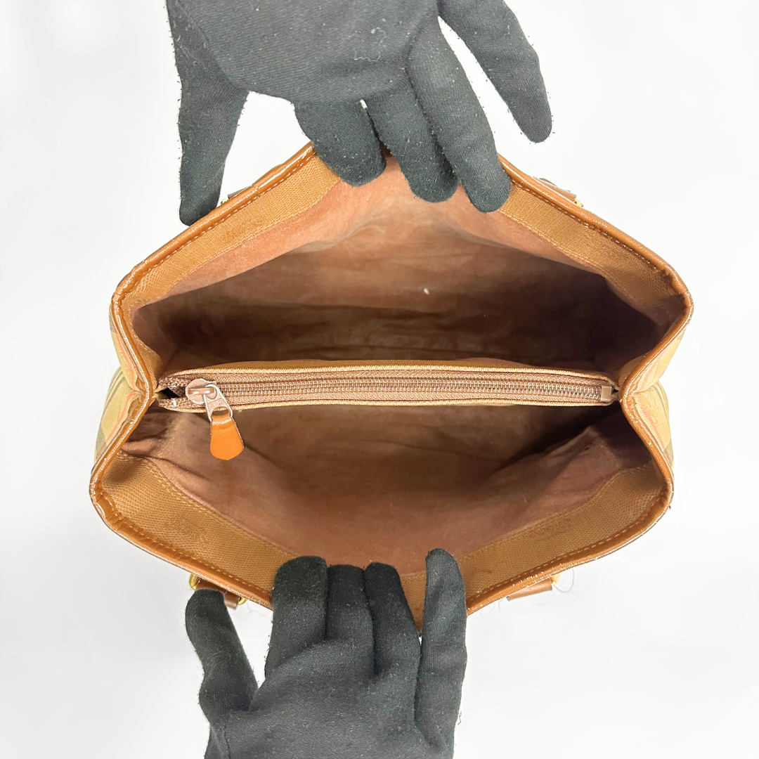 Brown leather bag with a zipper being held open by gloved hands on a white background