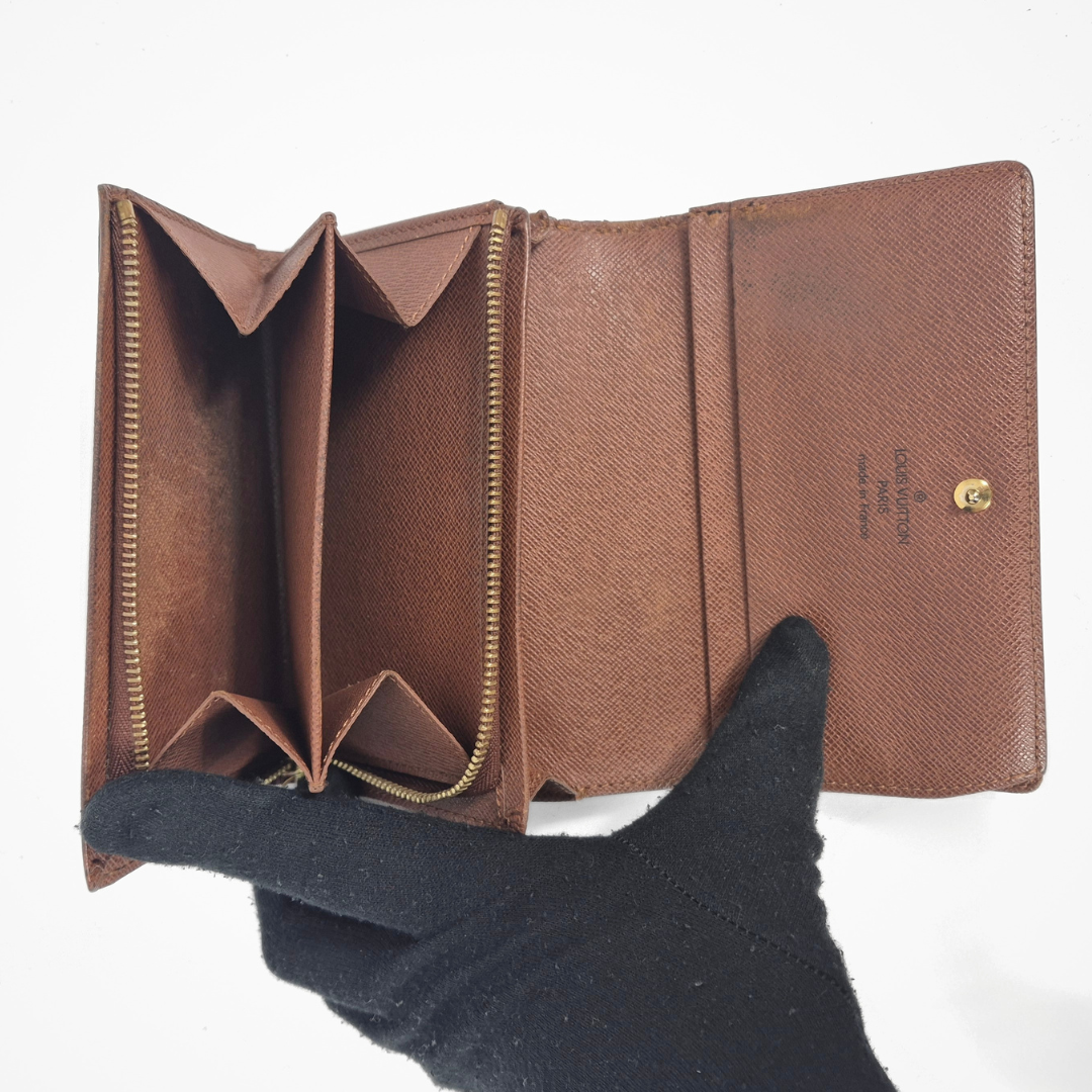 Brown leather wallet held open by a black-gloved hand on a white background