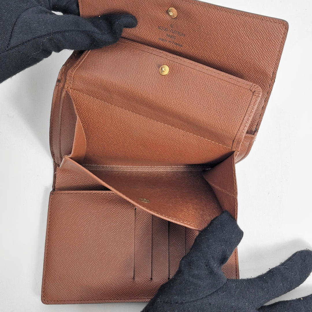 Brown leather wallet held open by a gloved hand on a white background