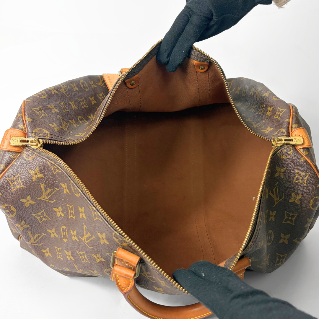 Brown hand bag with orange accents and a prominent logo pattern on a white background