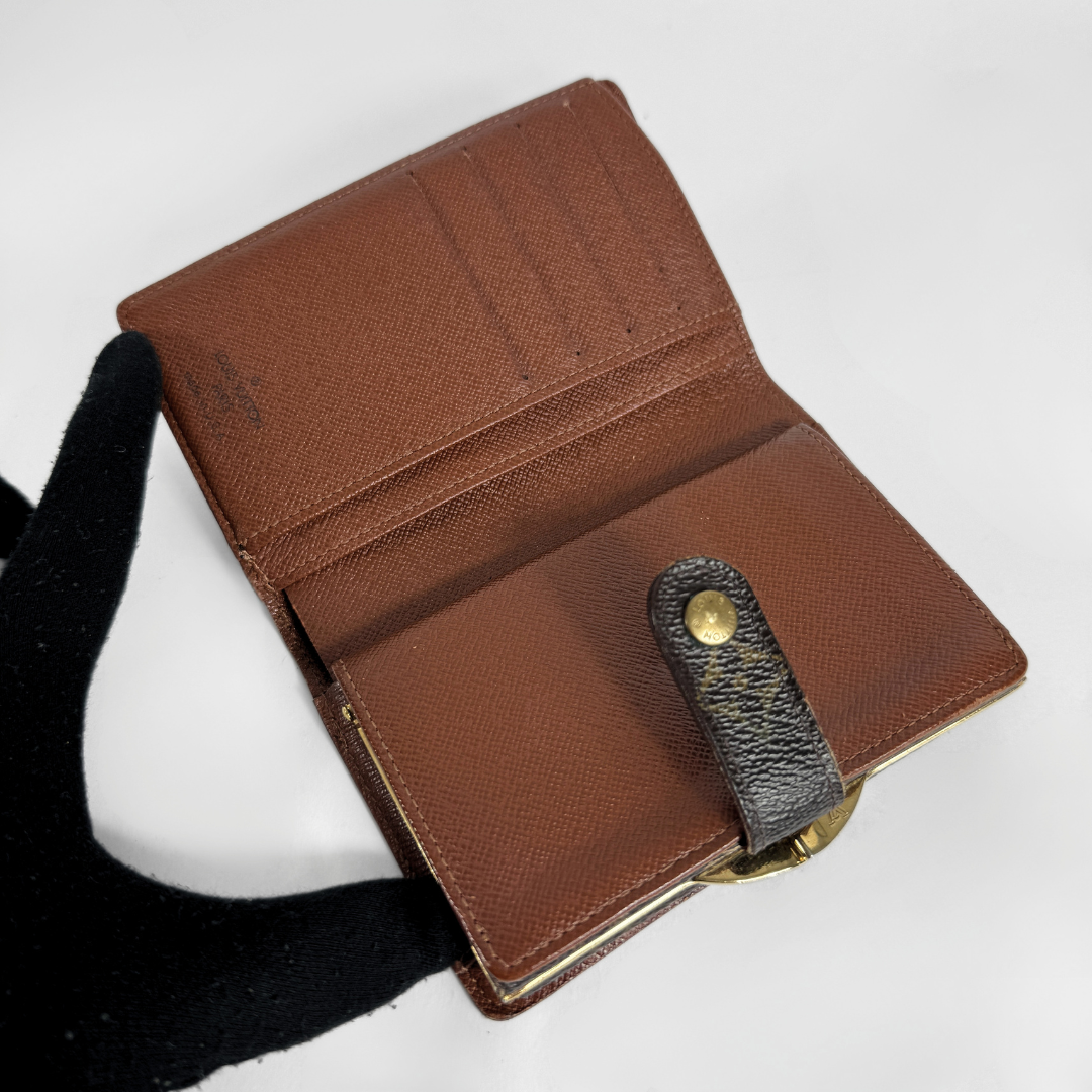A brown pebbled leather bi-fold wallet shown open, revealing card slots and interior compartments. A black textured strap with a gold-tone snap button is attached on the front.
