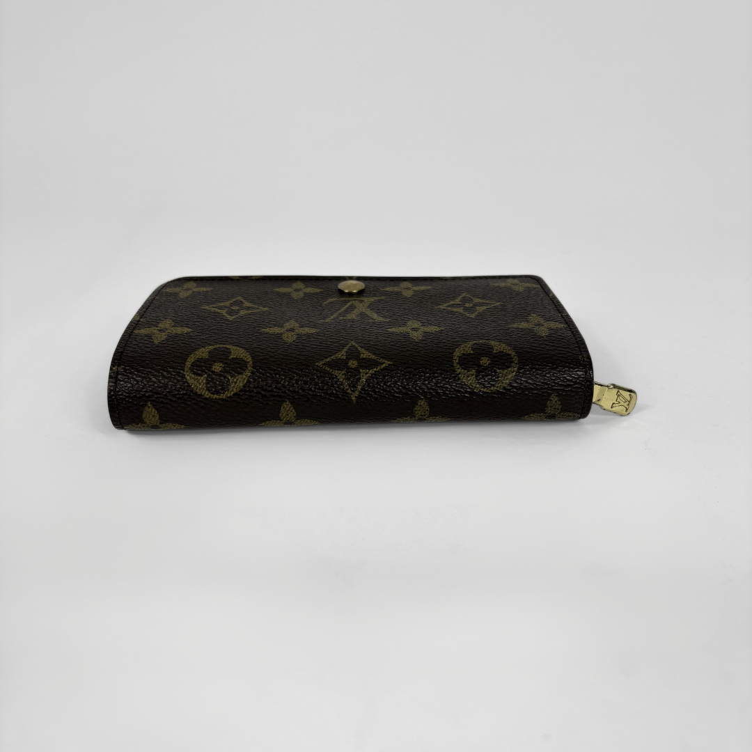 Louis Vuitton monogram canvas zip-around wallet in dark brown with gold-tone hardware, photographed on a light gray background.