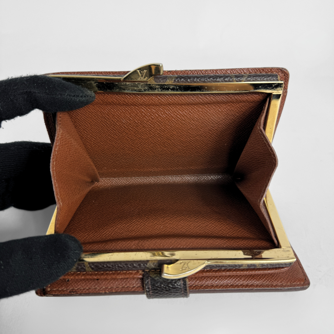A brown textured leather clutch wallet with gold-tone metal frame hardware, held open by a hand wearing a black glove against a plain white background.