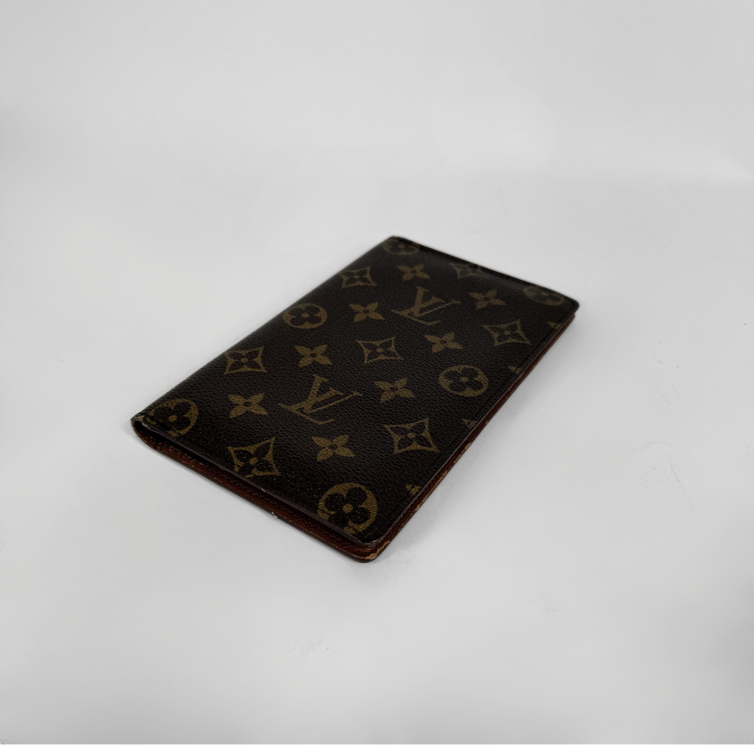 A Louis Vuitton monogram card holder in dark brown coated canvas with the classic tan/gold LV and floral motifs, shown on a plain light gray background.