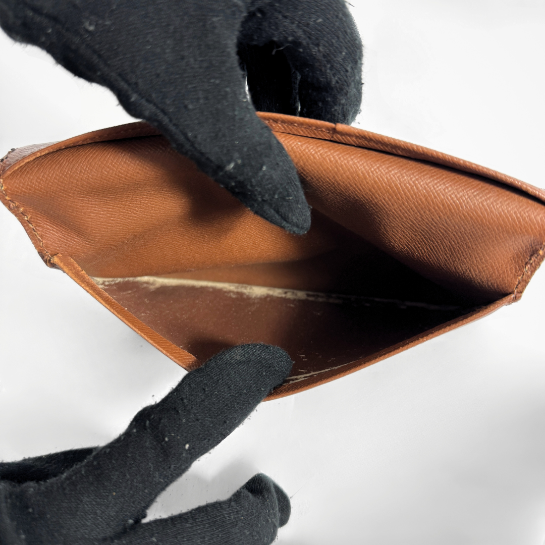 A close-up of a brown leather card holder or wallet being held open by two black gloves against a plain white background.
