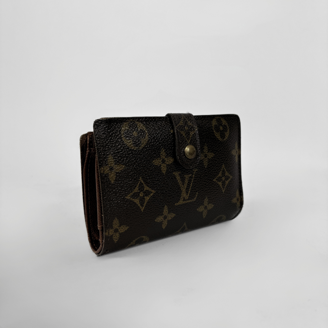 A Louis Vuitton monogram canvas bi-fold wallet in dark brown with gold-tone hardware, photographed on a light gray background.