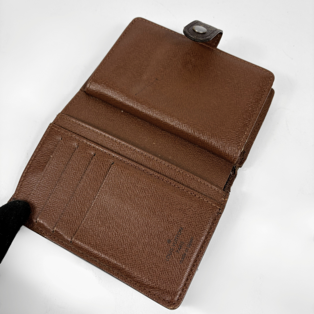 A brown textured leather wallet shown open, revealing multiple card slots and a small black snap tab at the top, photographed on a plain white background.