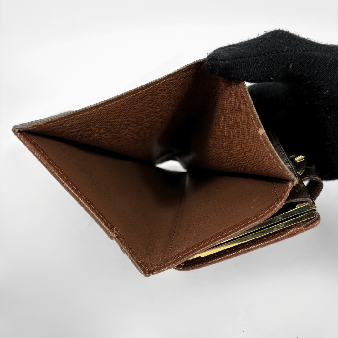 A brown leather bifold wallet held open by a black gloved hand, showing the interior card slots and gold-tone metal clasp against a plain white background.