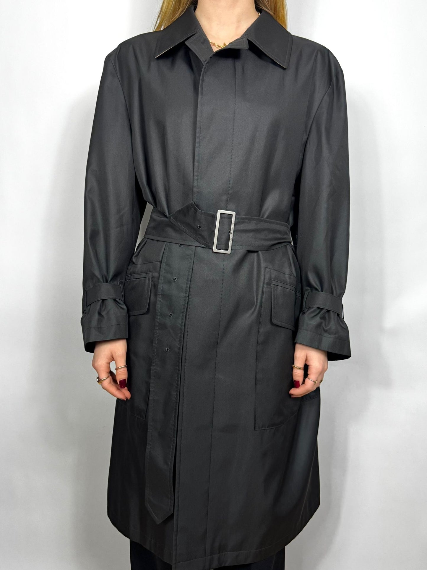 Person wearing a long black coat with a belt on a white background