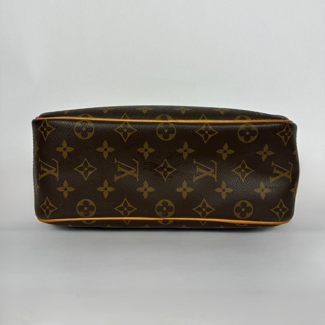 A Louis Vuitton monogram canvas bag shown from the side, featuring the classic brown and gold monogram pattern with tan leather piping along the edges, set against a plain light gray background.