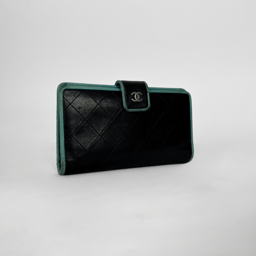 A black quilted leather wallet with green trim and a silver-tone interlocking CC logo on the front flap, photographed on a light gray studio background.