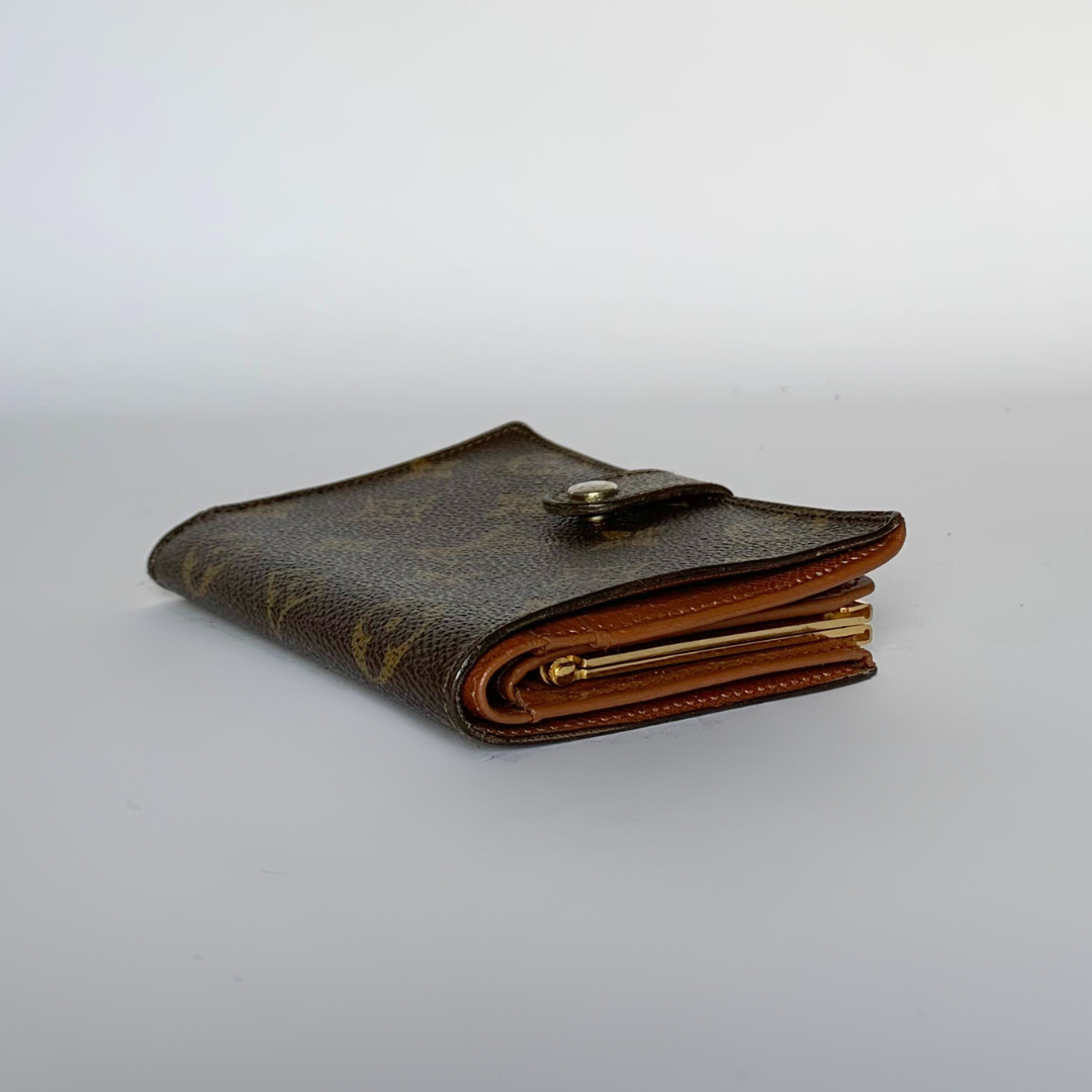 A classic Louis Vuitton monogram bifold wallet in brown coated canvas with tan leather edges and gold-tone metal hardware, photographed on a light gray studio background.