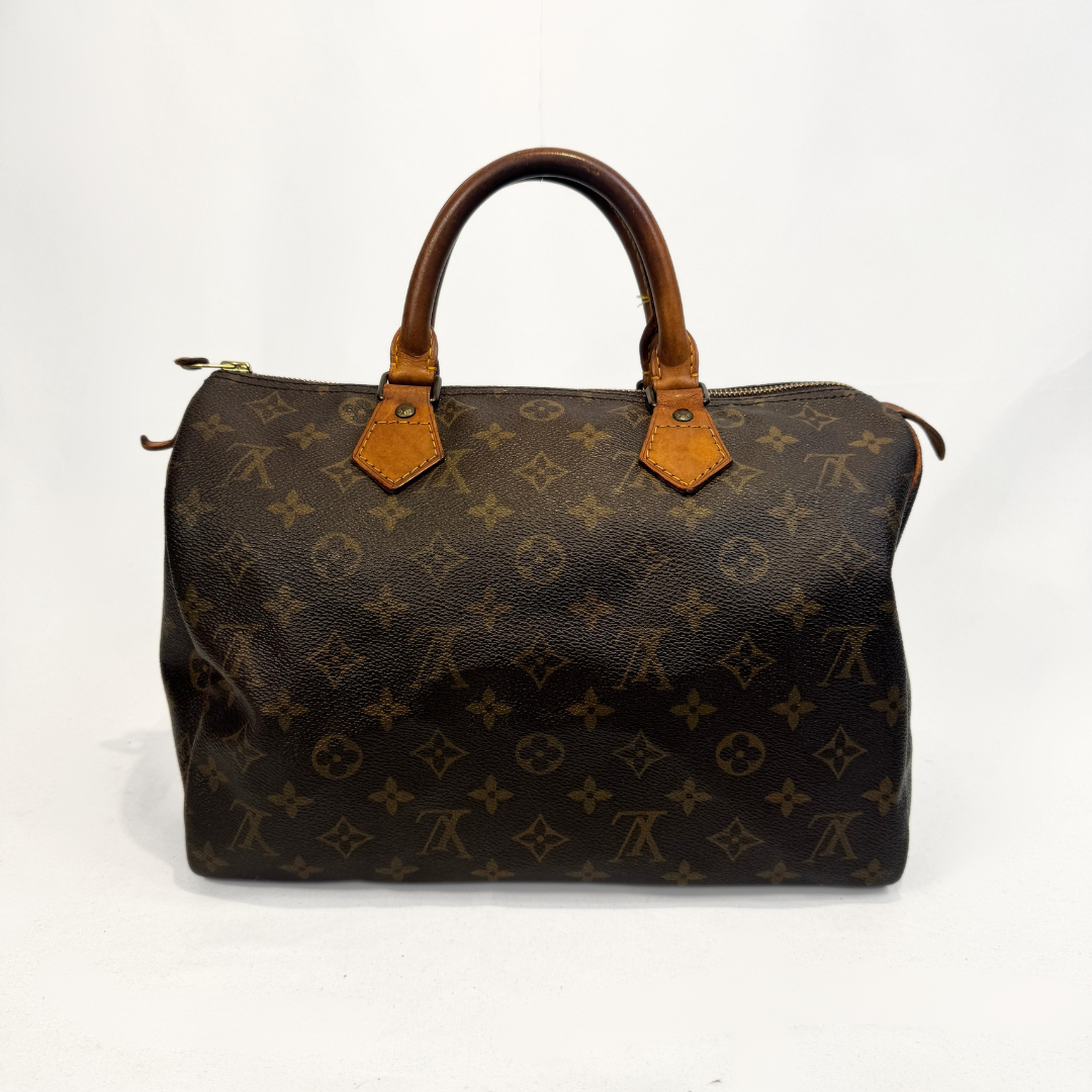 A Louis Vuitton monogram canvas Speedy handbag in dark brown with tan leather handles and trim, photographed against a light gray studio background.