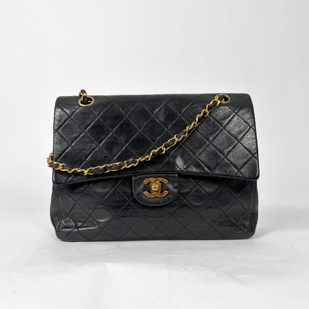 Black quilted handbag with gold chain and clasp on a white background