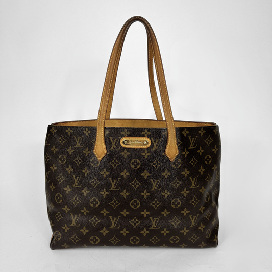 Louis Vuitton monogram canvas tote bag with tan leather handles and a gold-tone metal logo plate, photographed against a plain light gray background.