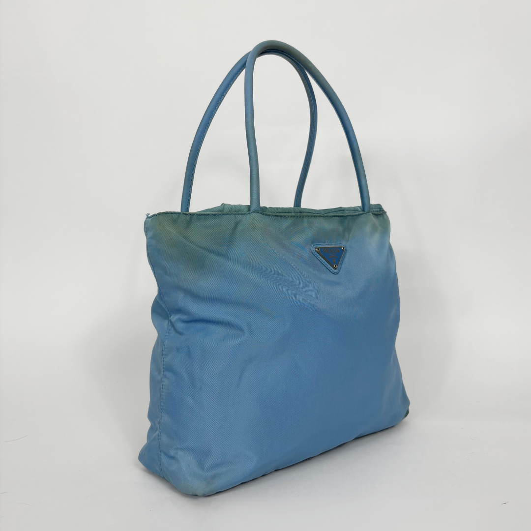 Prada light blue nylon tote bag with matching top handles and the signature enamel triangle logo.