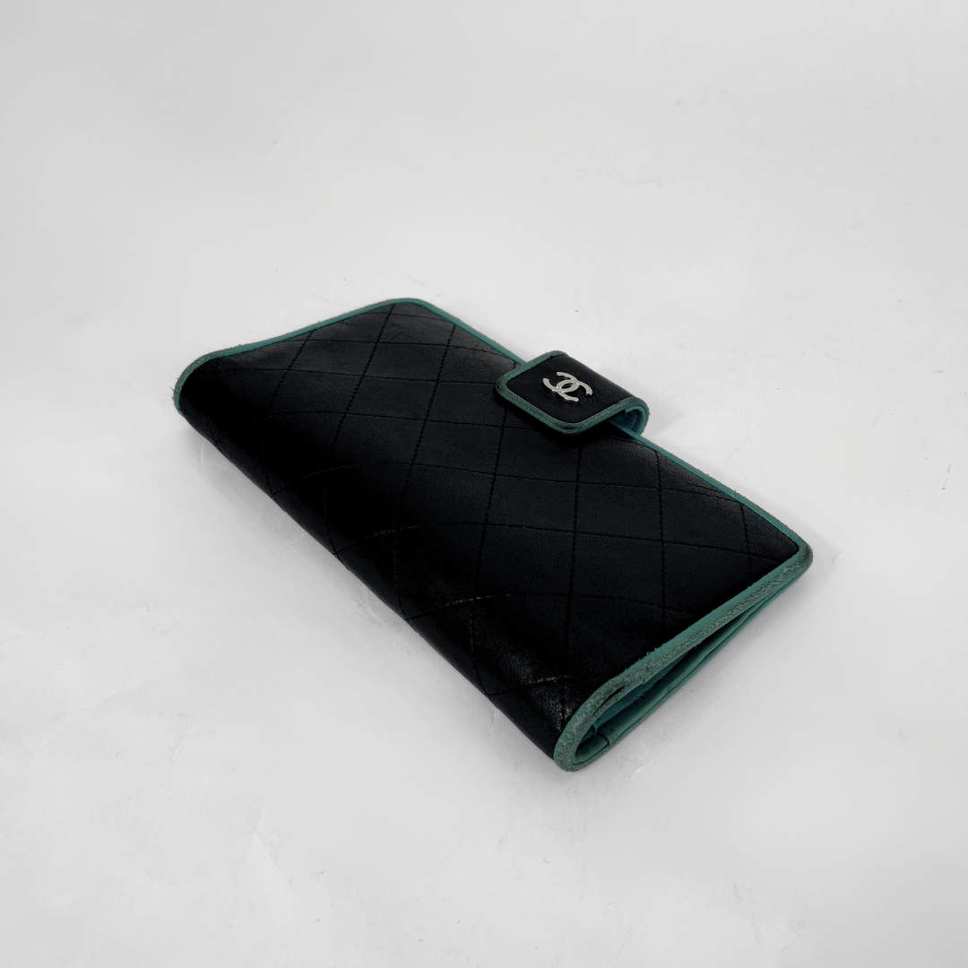 A black quilted leather wallet with dark green trim and a small black flap closure featuring a silver interlocking CC logo, photographed on a light gray background.