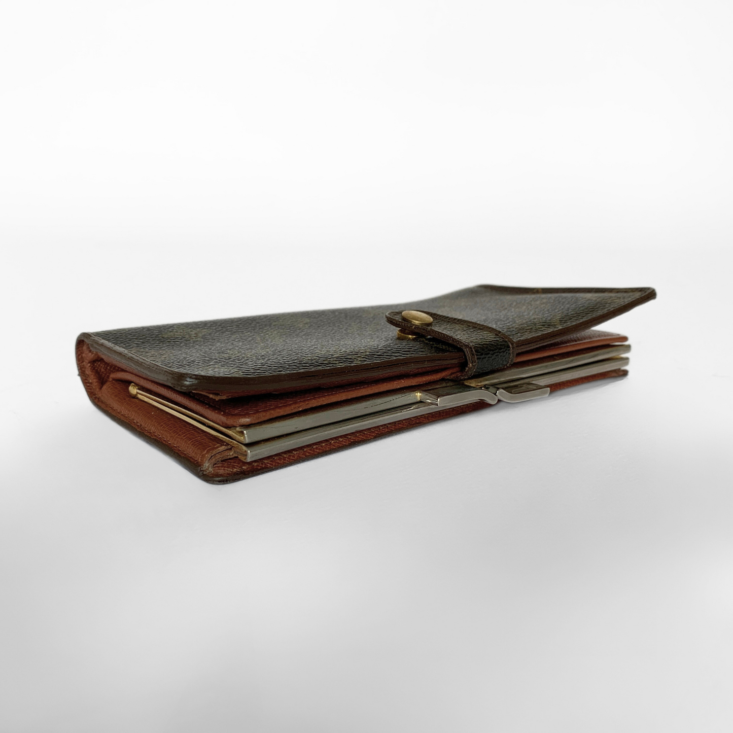 A dark brown leather wallet with a strap closure and brass button, shown open to reveal interior card slots and a silver metal clasp, photographed on a light gray studio background.