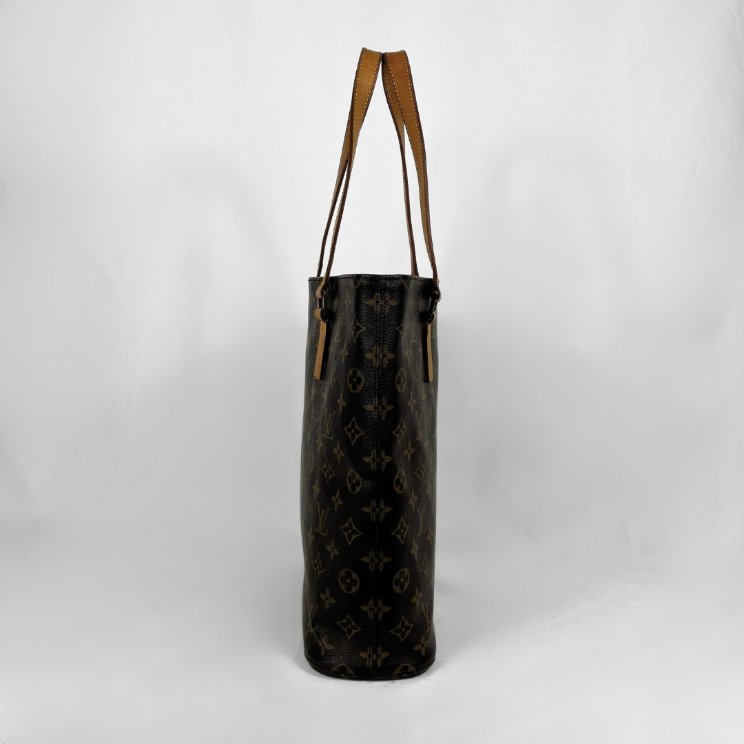 A Louis Vuitton monogram canvas tote bag with brown leather shoulder straps, standing upright against a light gray studio background.