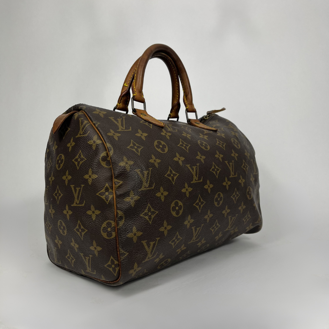 A Louis Vuitton monogram canvas speedy bag with brown leather handles and trim, photographed on a light gray studio background.