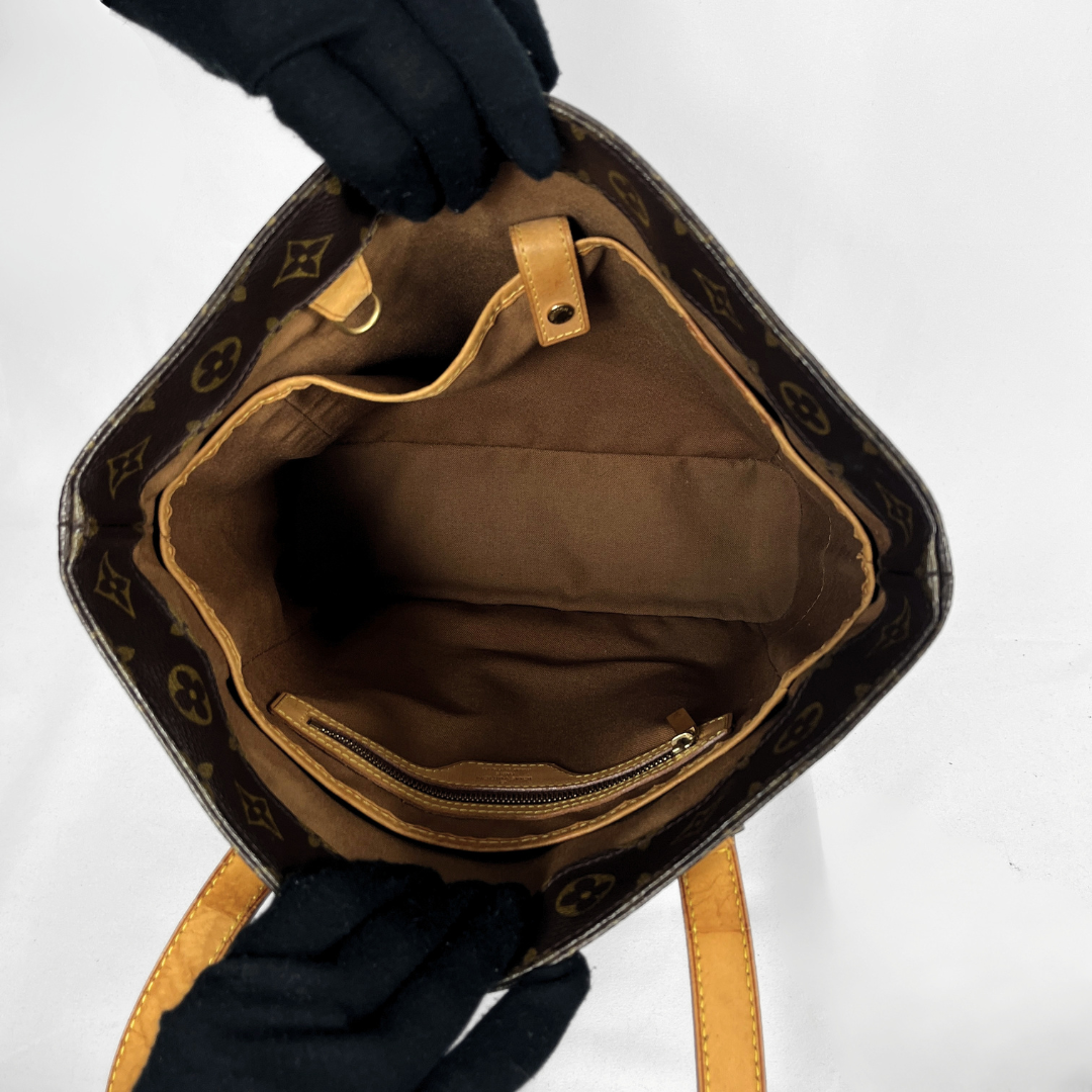 An open Louis Vuitton monogram bucket bag shown from the inside, with black gloved hands holding it open against a plain white background.
