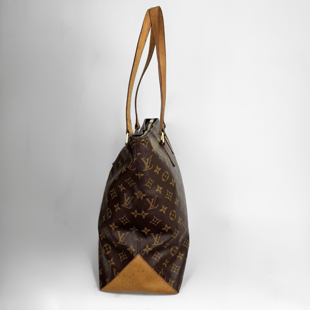 A Louis Vuitton monogram canvas tote bag with tan leather trim and shoulder straps, shown from a side profile view against a light gray background.