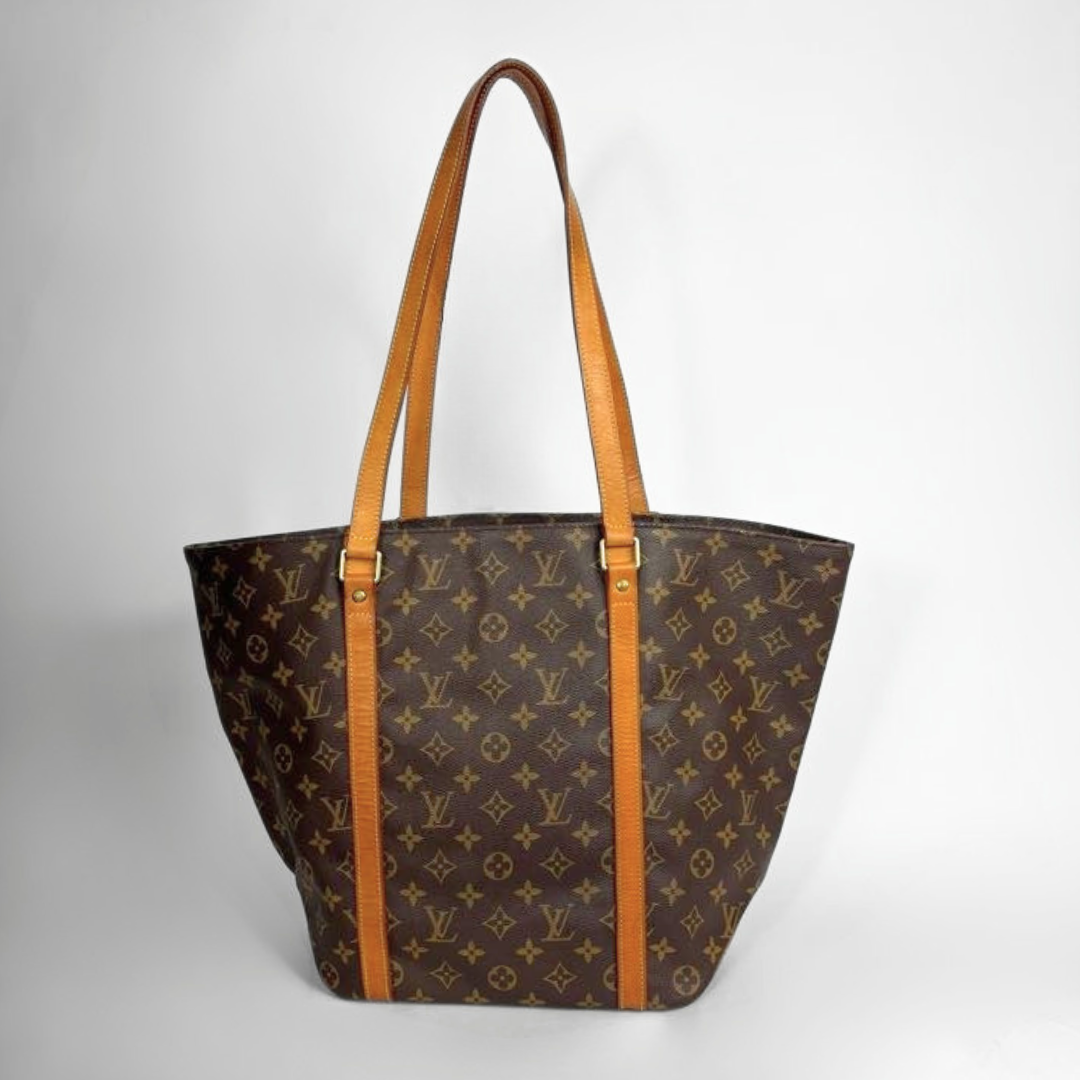 A Louis Vuitton monogram tote bag in brown coated canvas with tan leather shoulder straps and trim, shown against a light gray studio background.