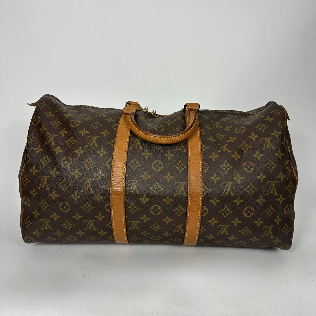 Brown monogram patterned duffel bag with tan leather straps on a white background