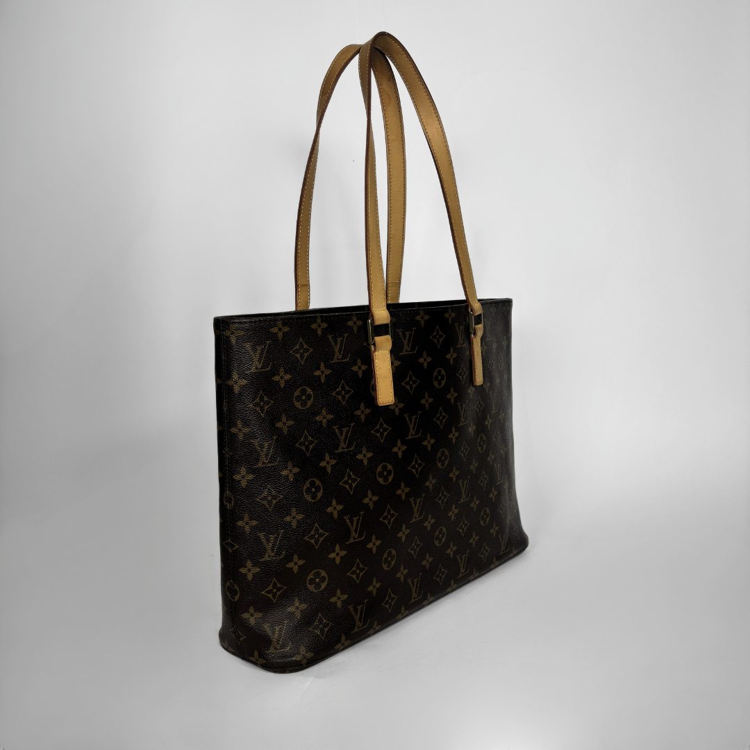 A Louis Vuitton monogram canvas tote bag with tan leather shoulder straps, shown from a three-quarters angle against a light gray studio background.