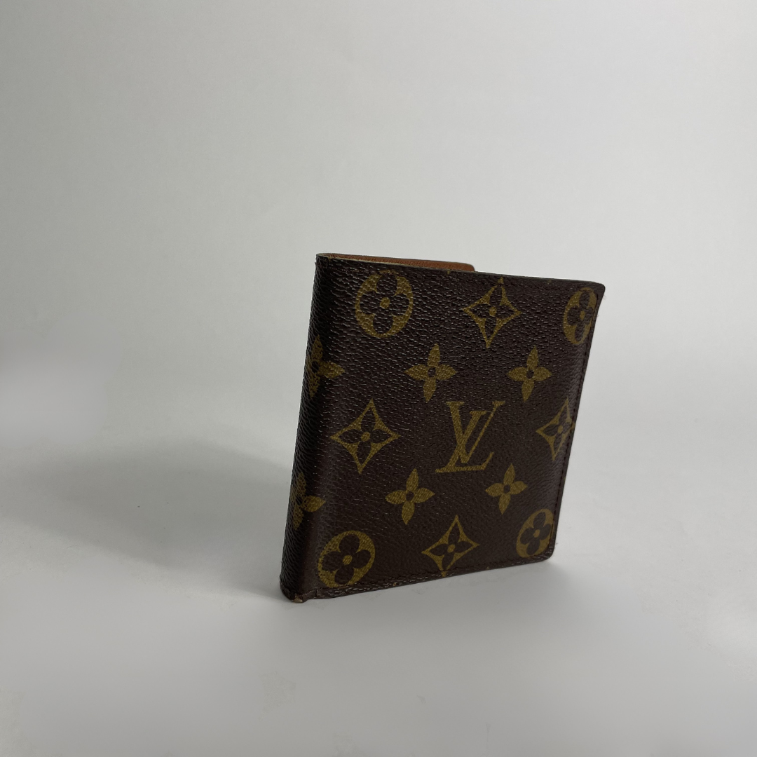 A small Louis Vuitton monogram wallet in brown coated canvas with gold-tone printed motifs, standing upright on a light gray studio background.