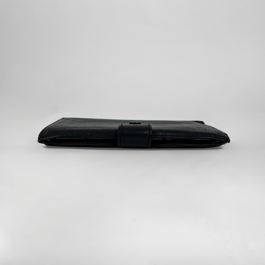A black textured leather wallet with a horizontal strap closure, shown closed on a light gray studio background.