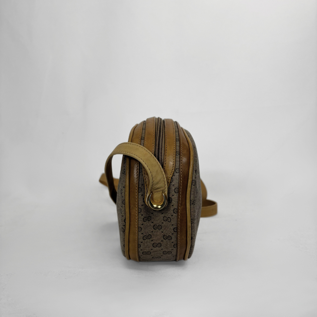 A vintage Gucci monogram shoulder bag in brown and beige canvas with tan leather trim and gold-tone hardware, shown from a side profile view against a plain white background.