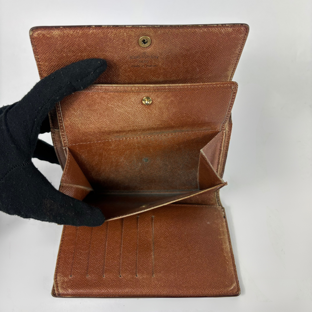 A brown textured leather wallet shown open, held by a black gloved hand against a plain white background.