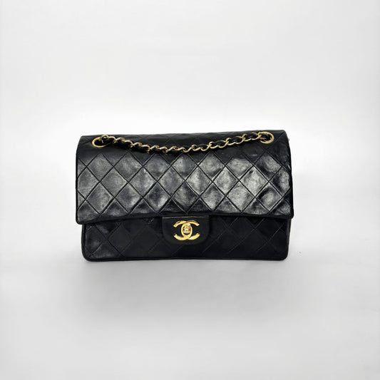 Black quilted handbag with gold chain and clasp on a white background