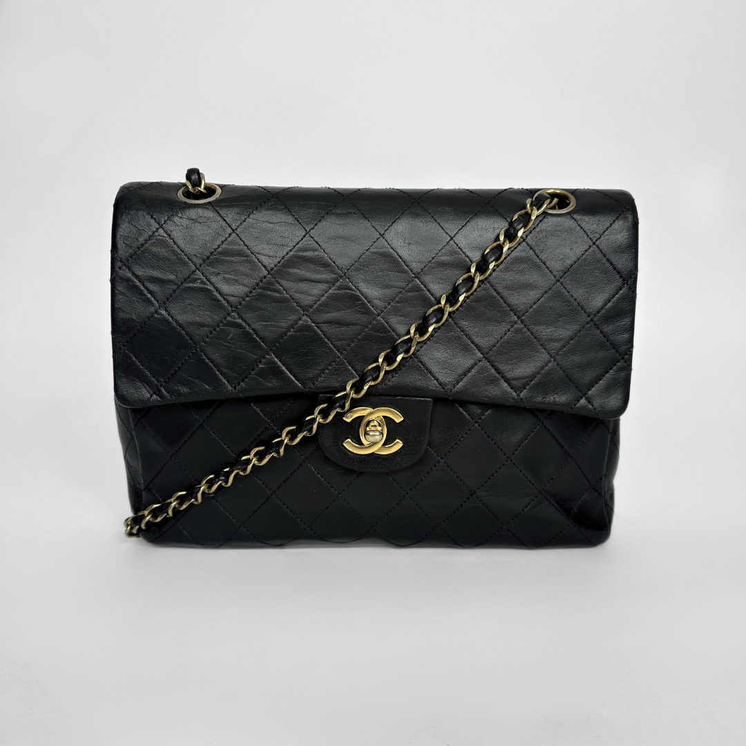 Black quilted handbag with gold chain and clasp on a white background