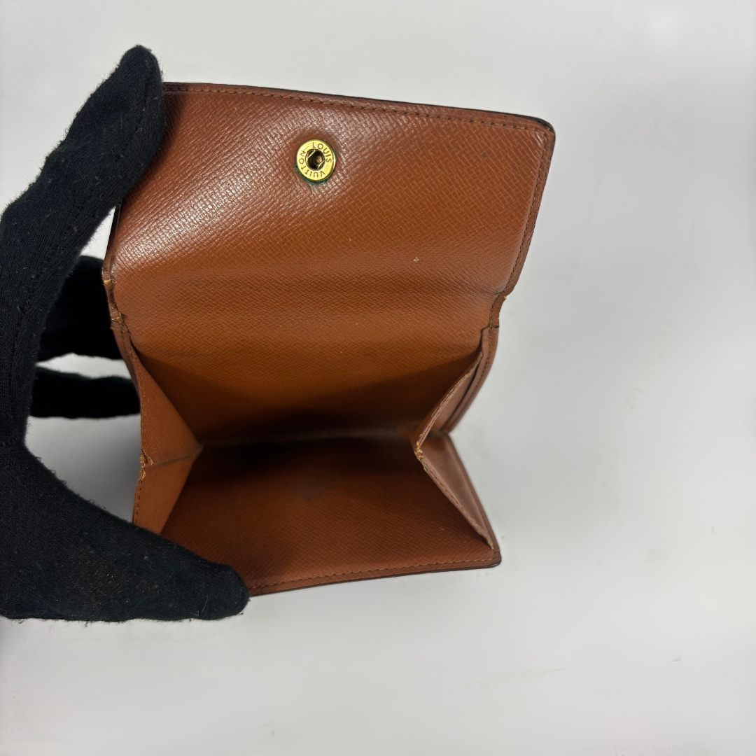 A brown textured leather wallet held open by a black gloved hand, showing its interior compartments and a small gold-tone snap button on a plain white background.