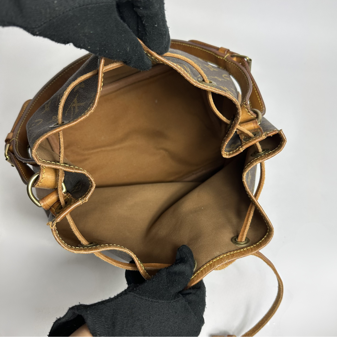Brown leather bag with gold accents held by a gloved hand on a white background
