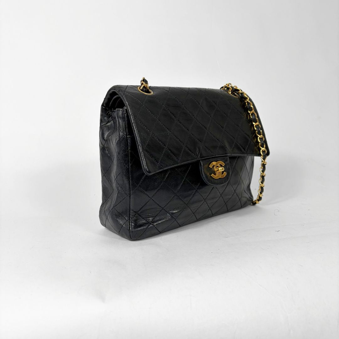 Black quilted handbag with gold chain and clasp on a white background