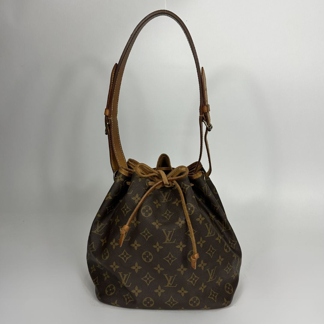 A Louis Vuitton monogram canvas bucket bag with a brown leather shoulder strap and drawstring closure, photographed against a neutral light gray background.