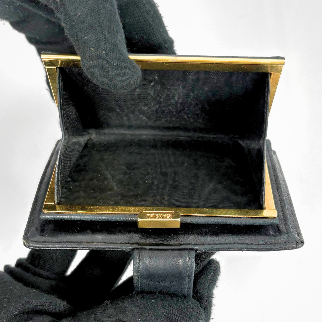 Black wallet with gold accents held by a gloved hand on a white background