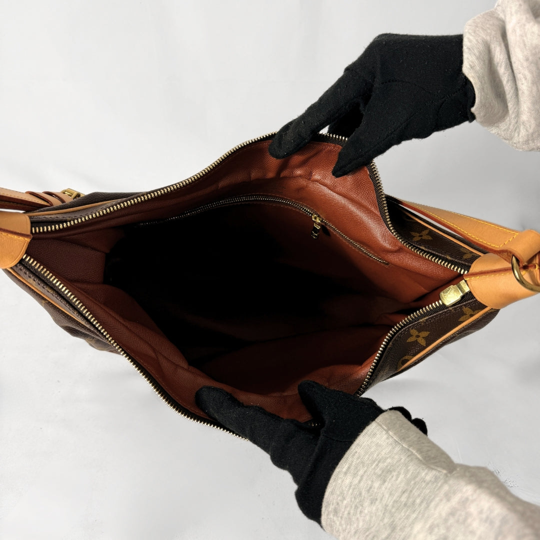A Louis Vuitton shoulder bag in brown monogram canvas and tan leather is shown open, with a person wearing black gloves holding the interior. The Louis Vuitton monogram pattern and gold-tone hardware are visible.
