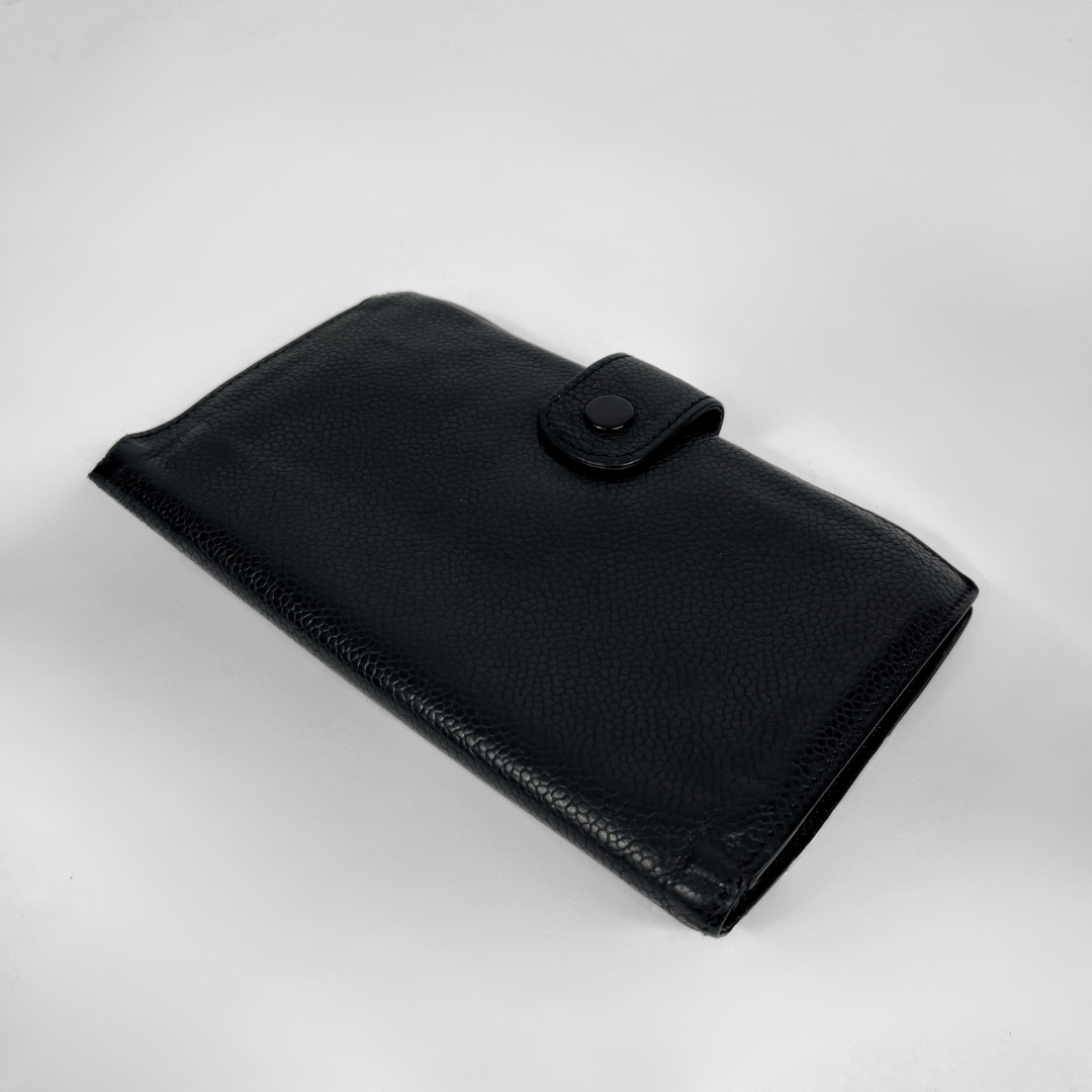 A black pebbled leather wallet with a snap-button closure, photographed on a light gray background.