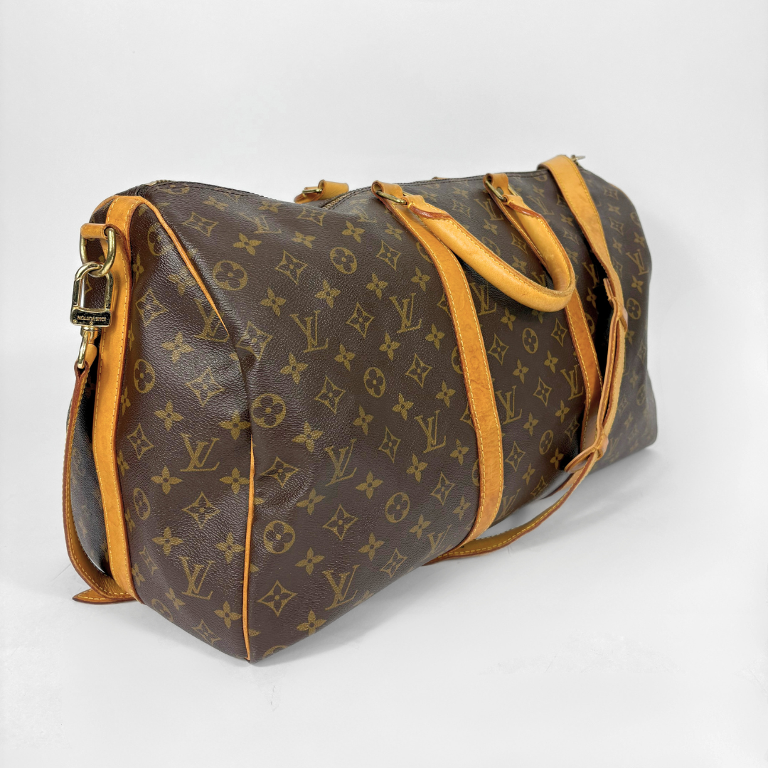 Louis Vuitton monogram travel bag with brown handles and strap on a white background