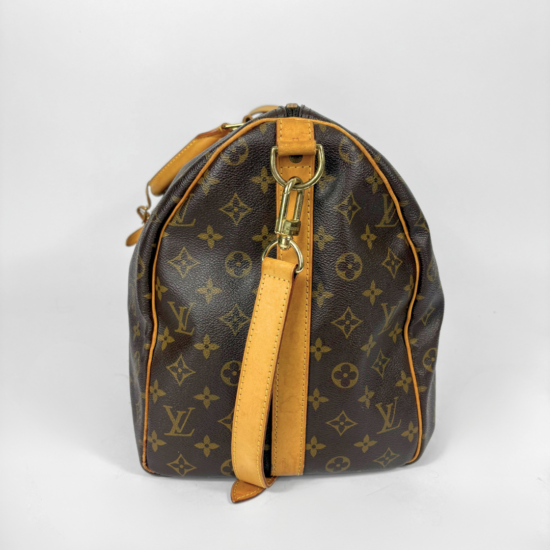 Louis Vuitton monogram travel bag with brown handles and strap on a white background