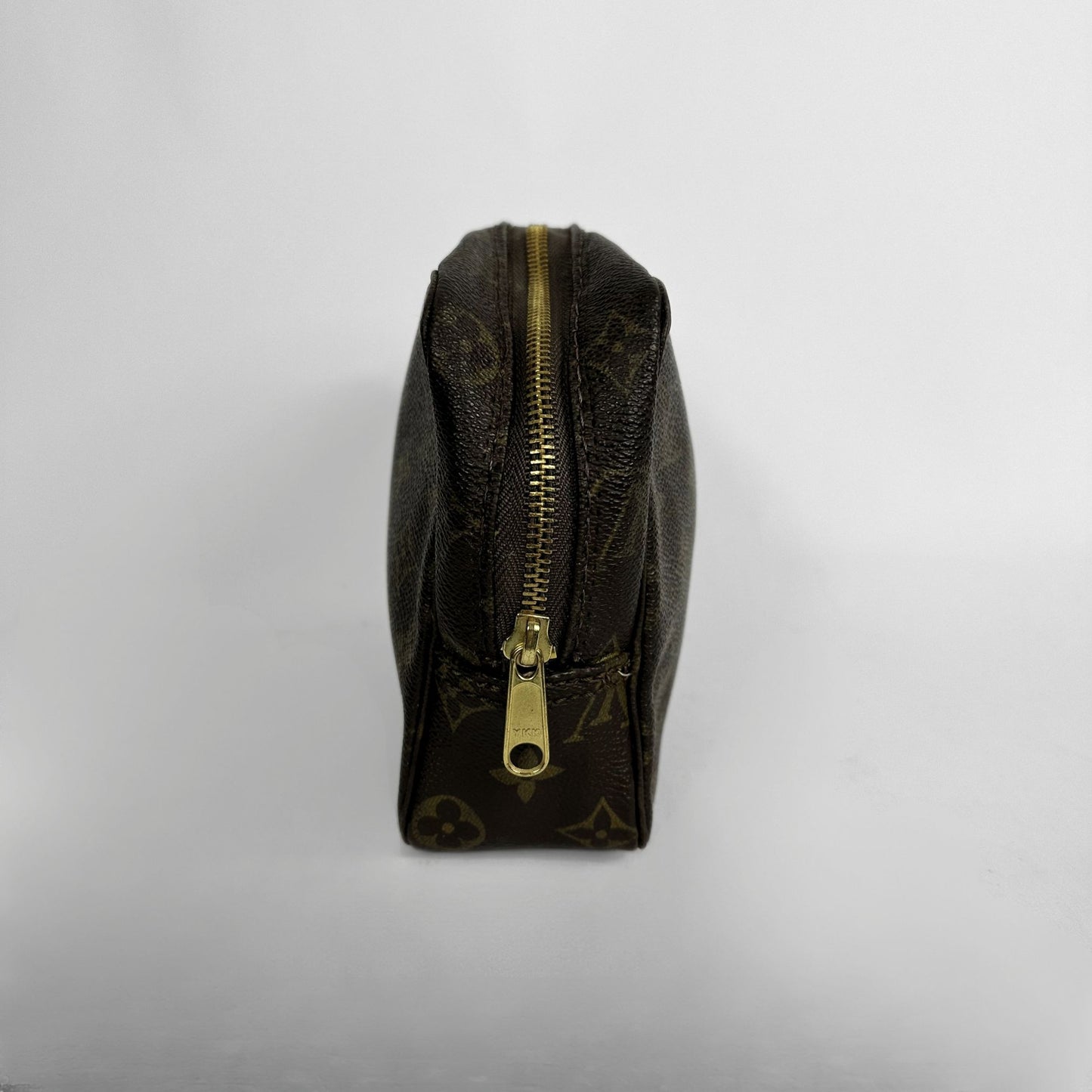 A Louis Vuitton monogram canvas zippered pouch shown from a side profile view against a plain light gray background.