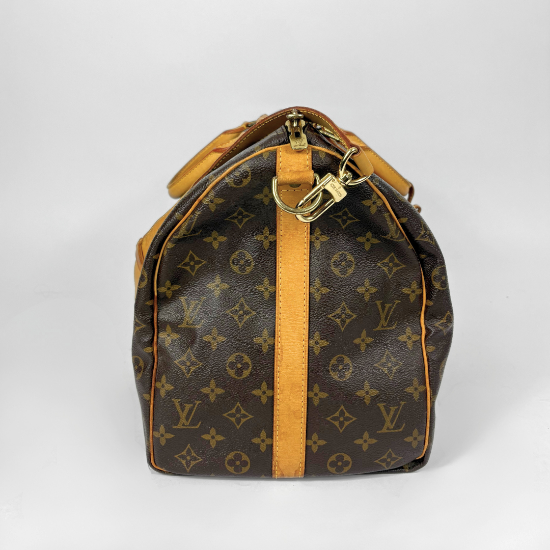 Louis Vuitton monogram travel bag with brown handles and strap on a white background