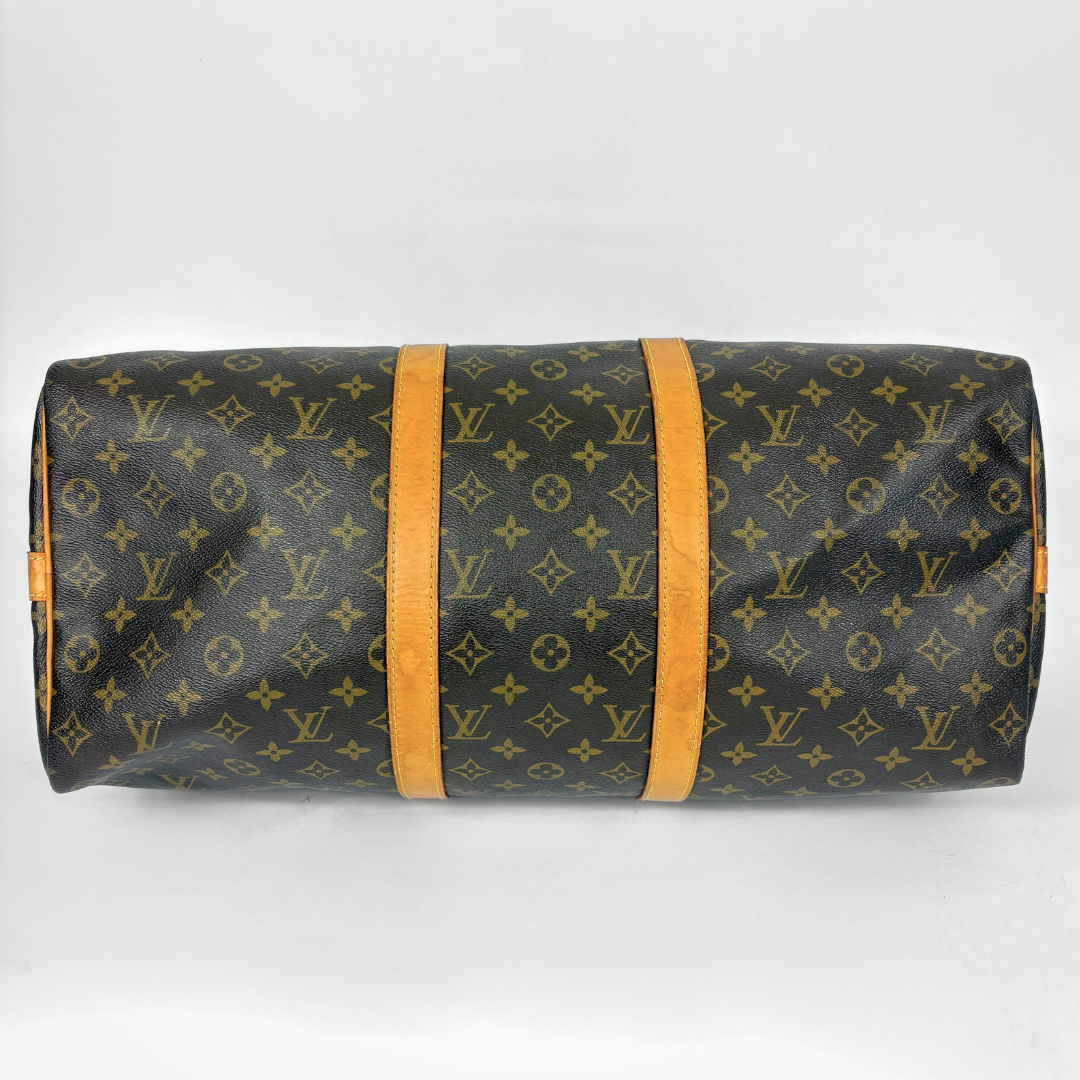 Louis Vuitton monogram travel bag with brown handles and strap on a white background