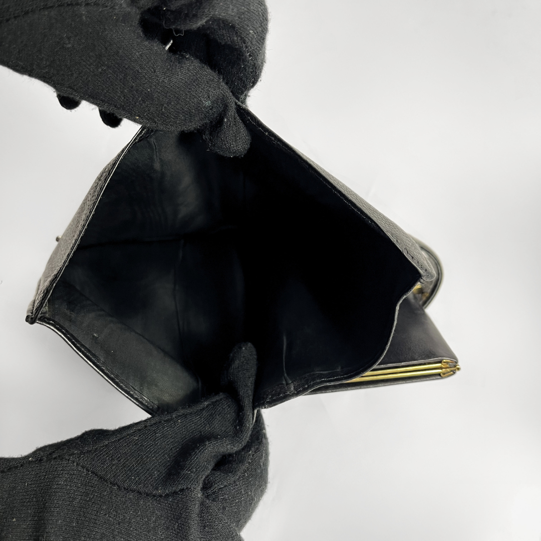 A black leather wallet or clutch shown open, held by black knit gloves against a plain light gray background.