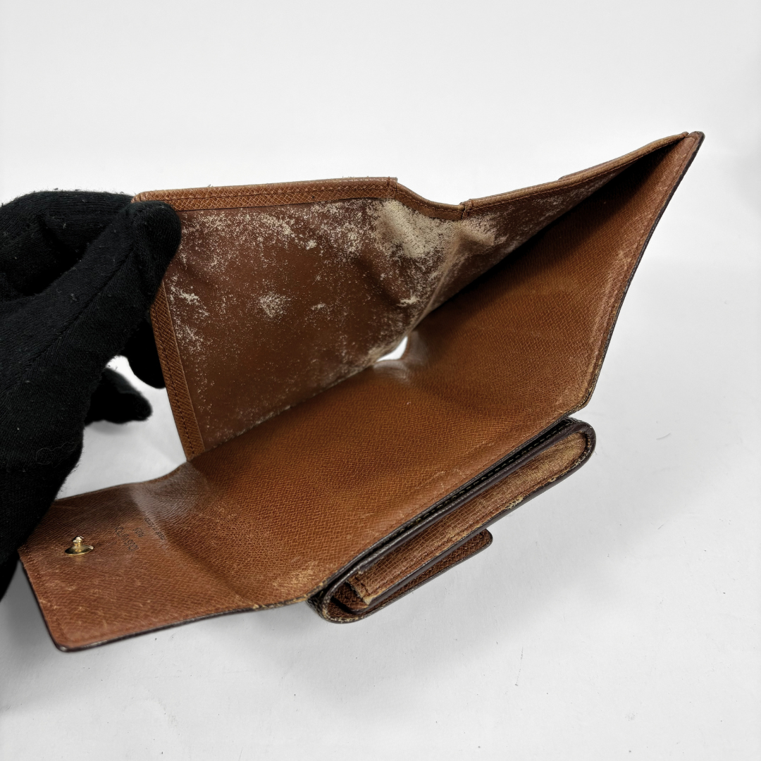A brown leather wallet held open by a black gloved hand, showing heavily dried white dust and lint inside on a plain white background.