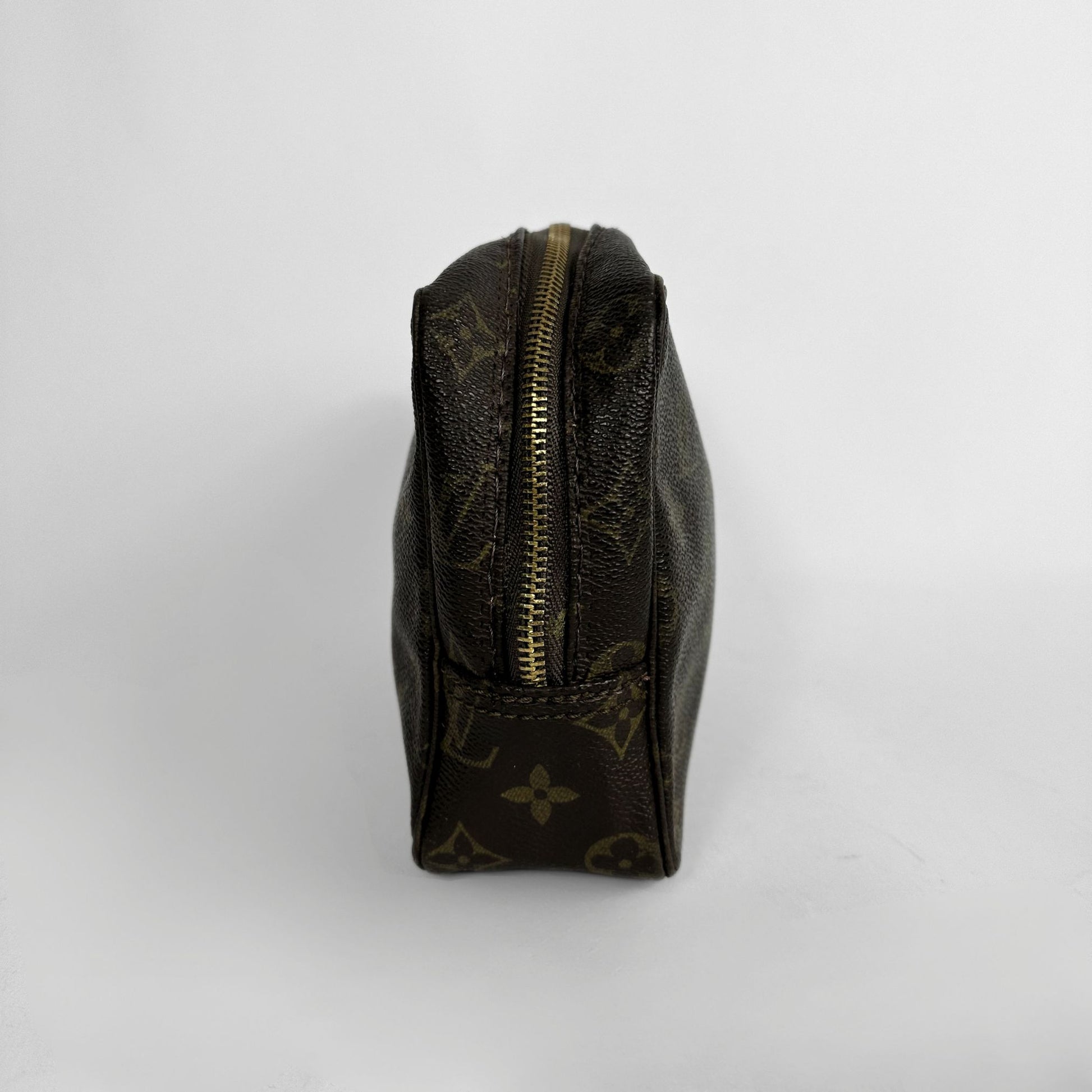 A Louis Vuitton monogram canvas pouch in dark brown with gold-toned hardware, photographed from the side against a light gray background.